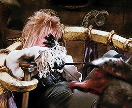 Gif of Jareth sitting in his thrown chair, looking like he's thinking and annoyed while a goblin runs across the frame
