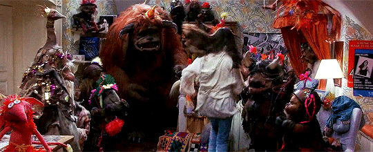 GIF of Sarah jumping onto her bed in her bedroom with many of the goblins and creatures she met during her journey through the labyrinth, including Ludo, Hoggle, Sir Didimus, the firyes, and several others. There are party streamers and the gabilns are dancing around.