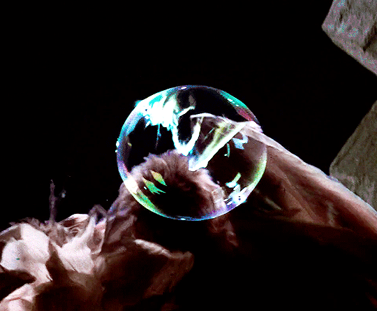 Gif of Sarah's hand reaching out for a bubble as it bursts while the white fabric of Jareth's owl robes flutter in the background